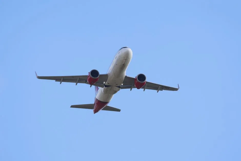 A commercial airplane soaring through a bright clear blue sky, captured from below.