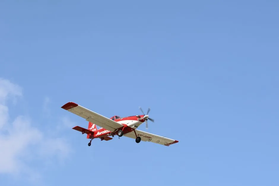 Red and white fixed-wing airplane soaring against a clear blue sky.